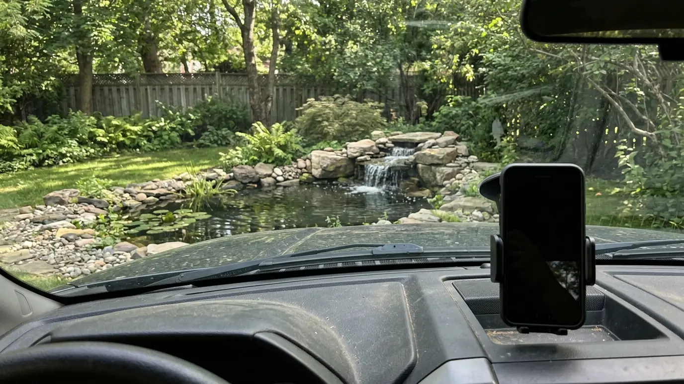 Call or send photos A phone mounted on a truck dashboard with a backyard and a garden pond visible through the windshield